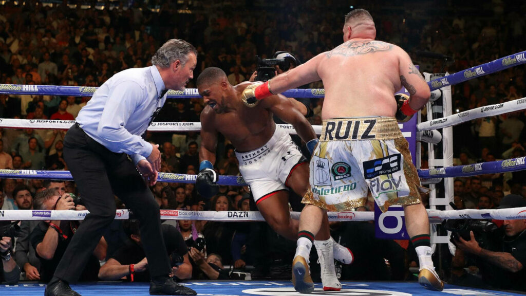 Andy Ruiz Jr. lands a powerful left straight punch in boxing ring with referee and crowd watching Wallpaper