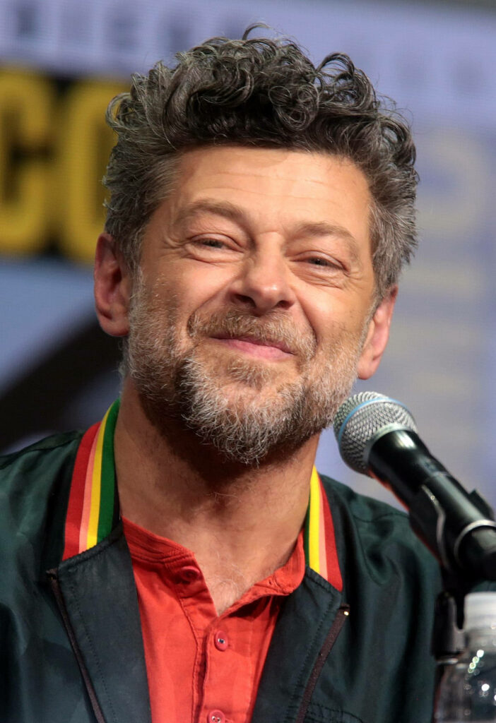 Andy Serkis smiling warmly speaking at Comic Con candid lively moment with wallpaper background