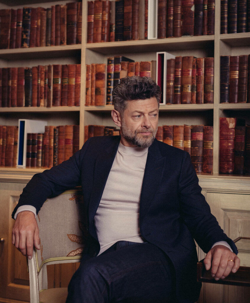 Andy Serkis sitting thoughtfully in a classic library surrounded by vintage books wallpaper background