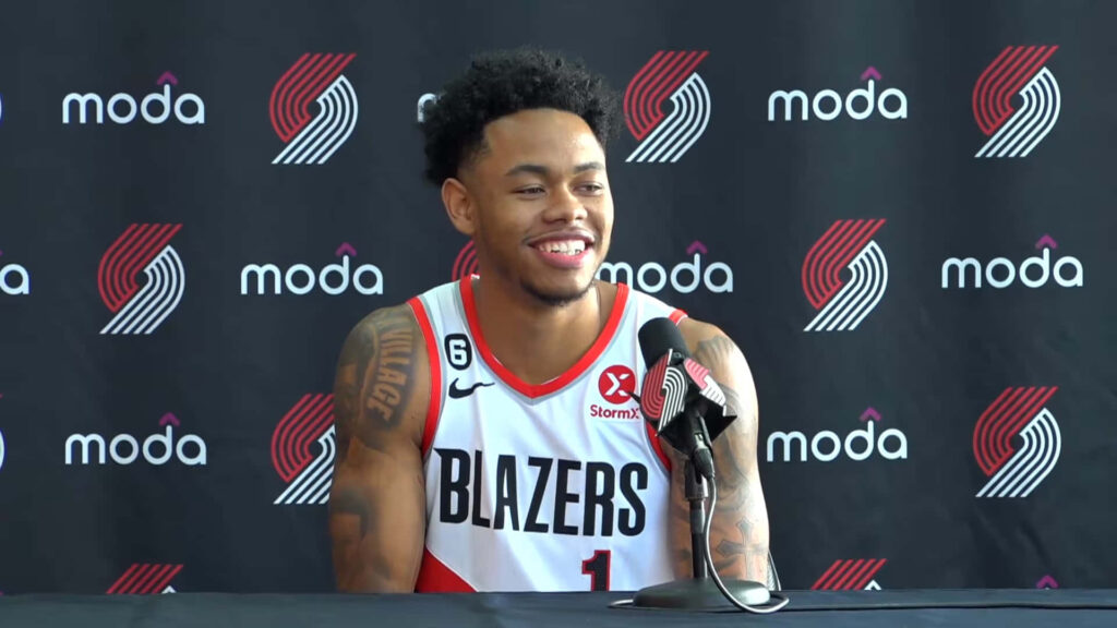 Anfernee Simons smiles in Portland Trail Blazers jersey at press conference with team logos background Wallpaper