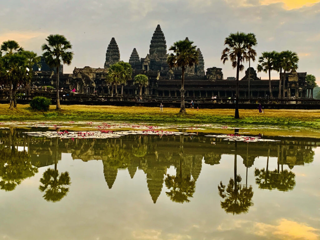 Reflection of Angkor Thom temple in calm water with palm trees and golden sky background Wallpaper