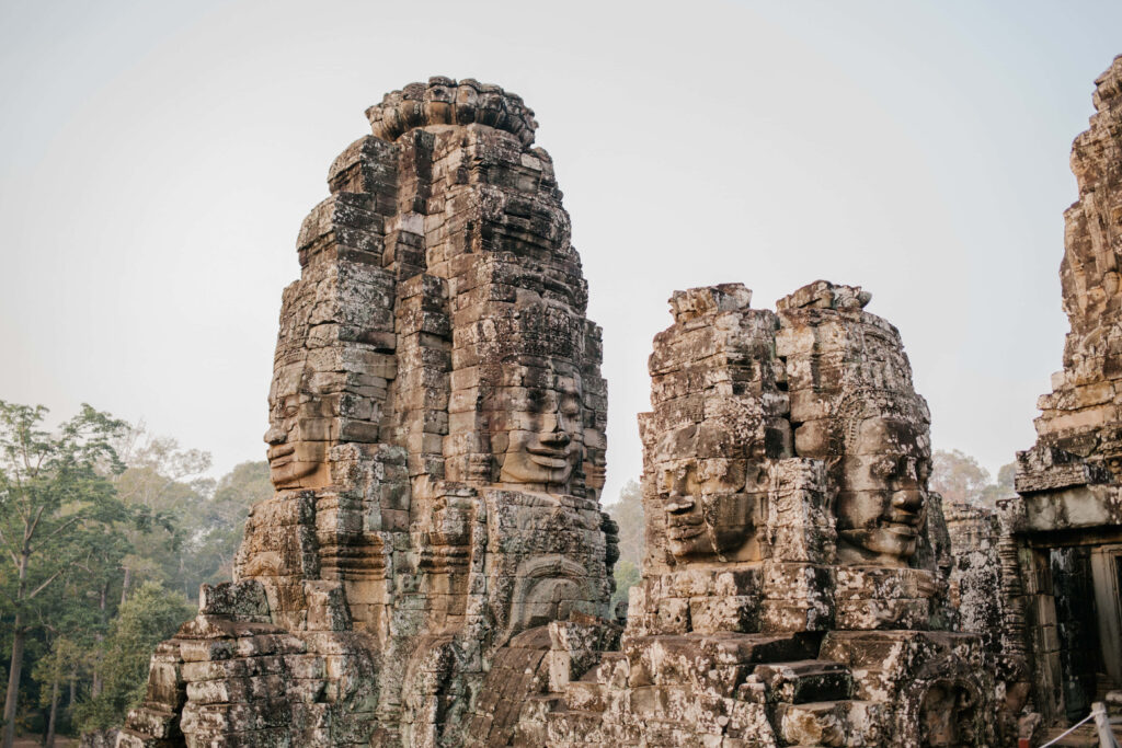 Stone faces and ancient architecture of Angkor Thom ruins surrounded by lush greenery wallpaper