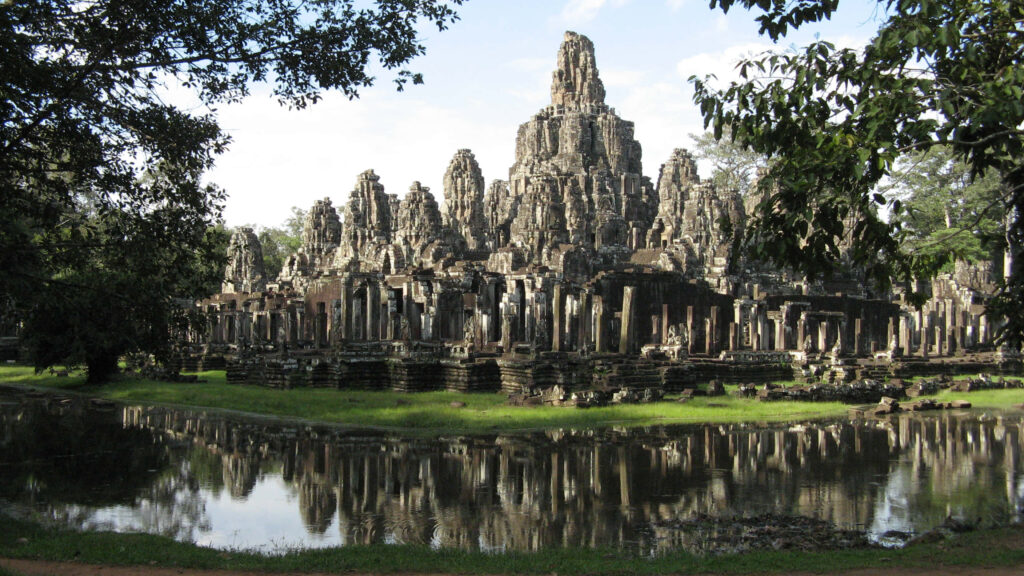 Ancient Angkor Thom stone towers reflected in tranquil pond with lush green surroundings wallpaper