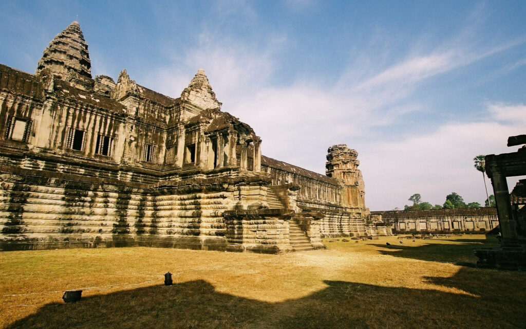 Ancient Angkor Wat temple ruins in Cambodia with intricate stone architecture under blue sky background Wallpaper