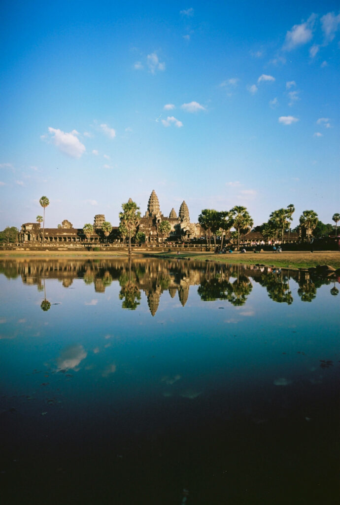 Angkor Wat temple with iconic towers and palm trees reflected in calm water under blue sky Wallpaper