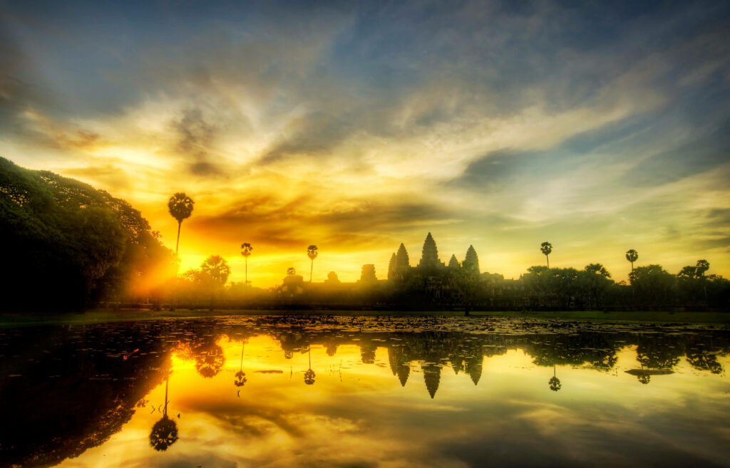Angkor Wat silhouette at sunset with palm trees reflected in calm water scenic wallpaper background