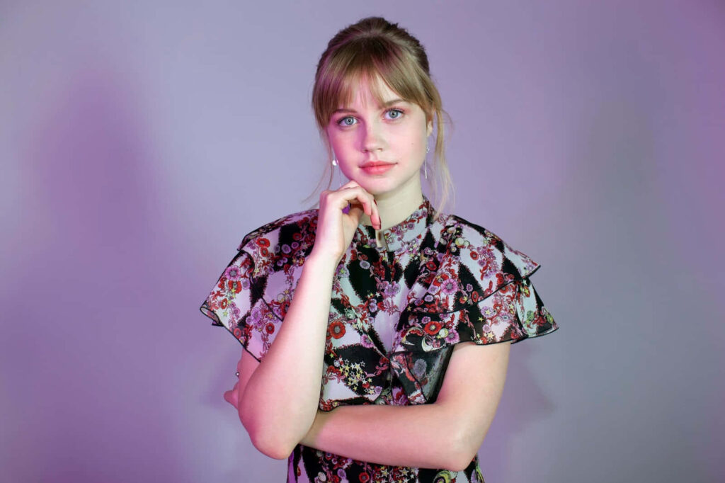 Angourie Rice in floral dress posing thoughtfully against soft purple elegant wallpaper background