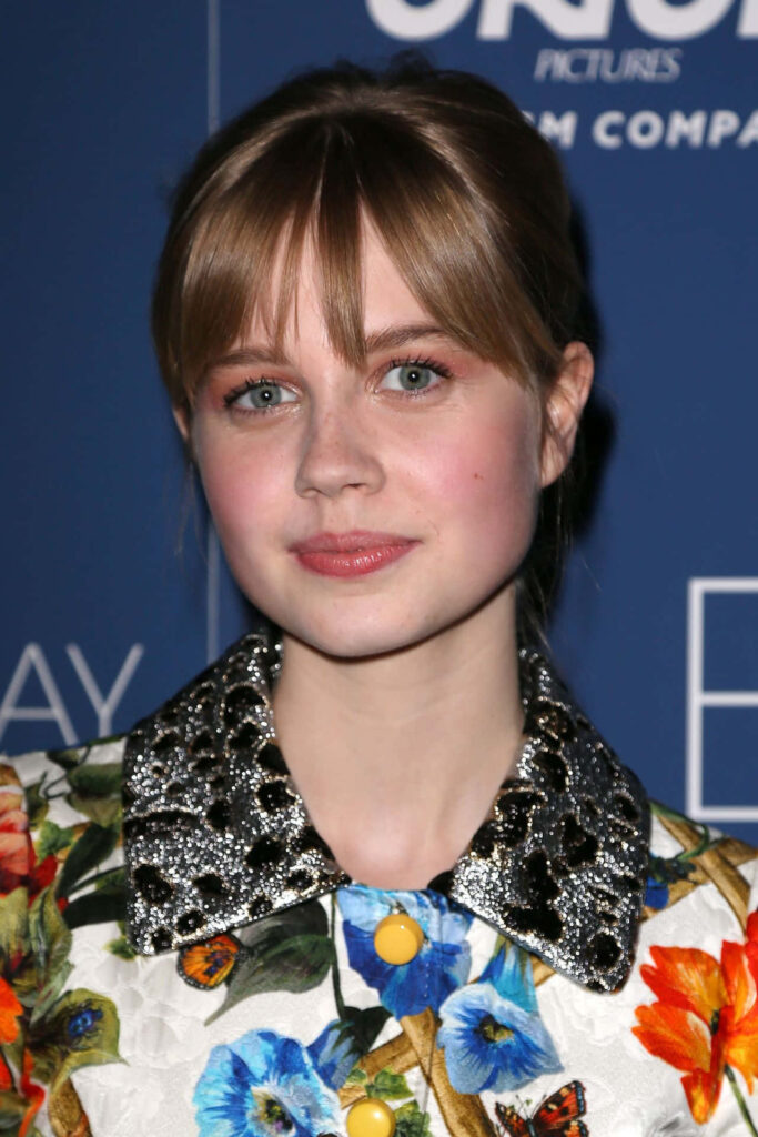 Angourie Rice in floral outfit with distinctive collar posing against blue event backdrop wallpaper