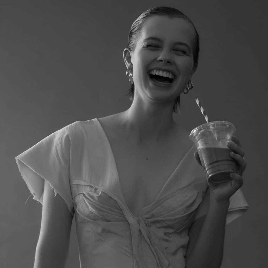 Angourie Rice smiling joyfully holding coffee cup bright wallpaper background atmosphere