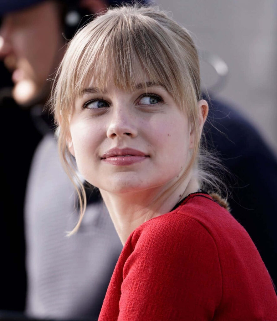 Angourie Rice in vibrant red top glancing over shoulder stylish captivating wallpaper background