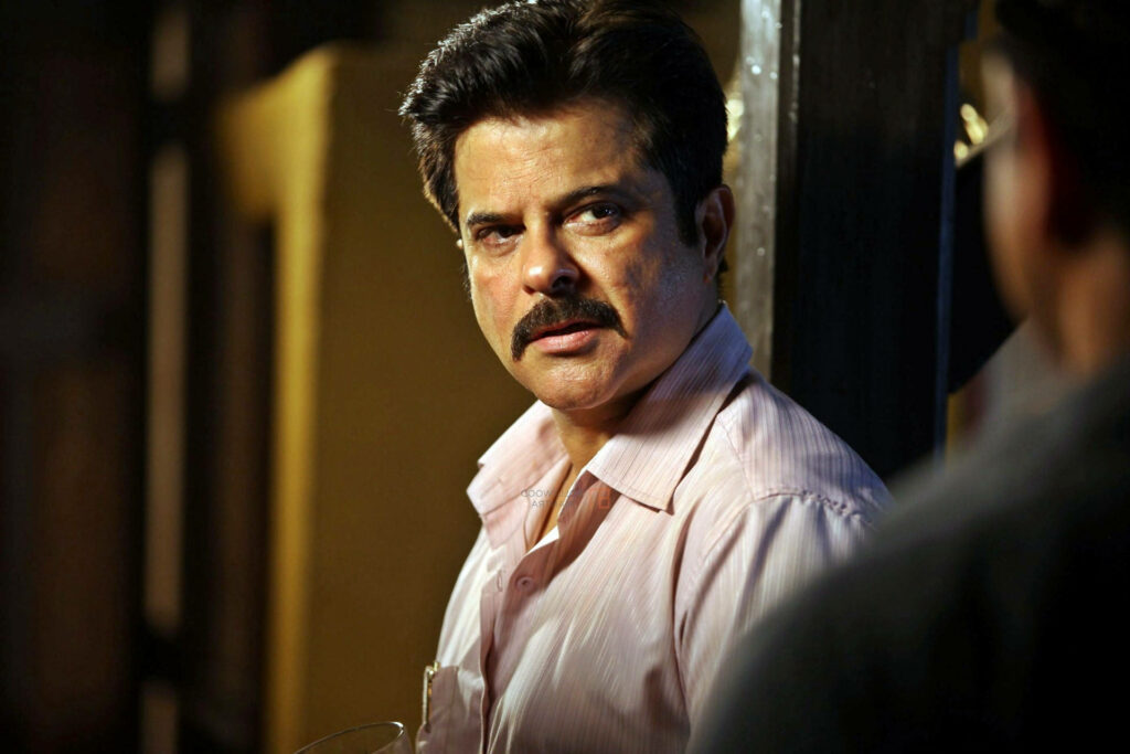 Anil Kapoor holding a drink looking intense sideways in a dramatic wallpaper background