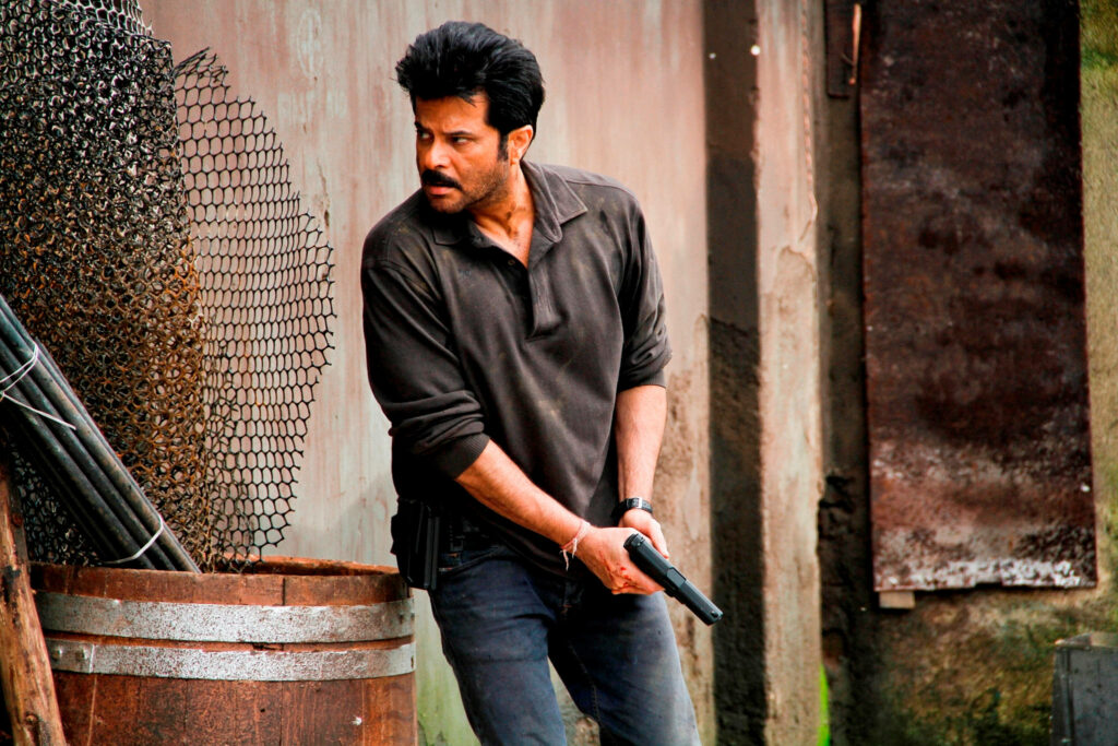 Anil Kapoor as Jai Singh Rathod in intense action pose holding gun against urban backdrop Wallpaper