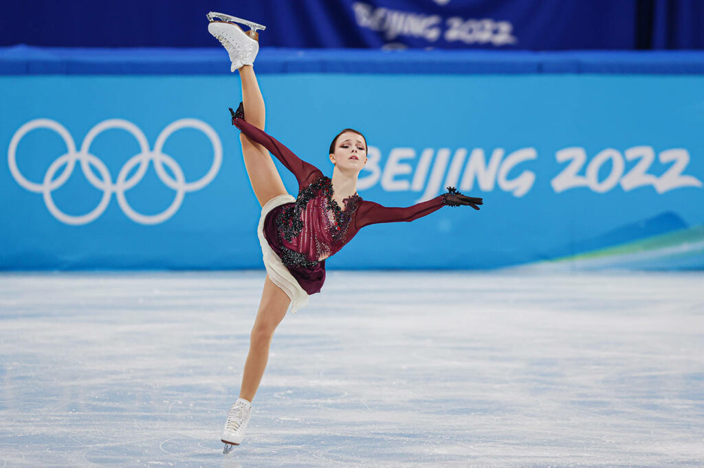 Anna Shcherbakova performing elegant athletic figure skating at 2022 Olympics with rings background Wallpaper