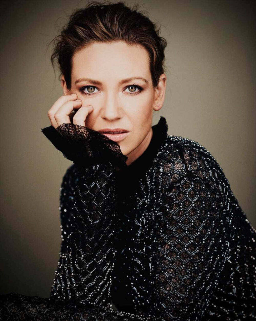 Anna Torv in elegant intricately patterned outfit posing thoughtfully against wallpaper background