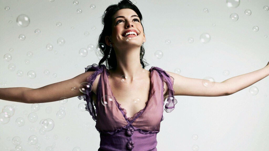 Anne Hathaway smiling joyfully surrounded by floating bubbles uplifting wallpaper background