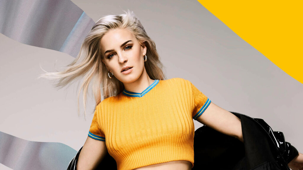Anne-Marie confident low-angle shot wearing vibrant yellow top with modern abstract wallpaper background