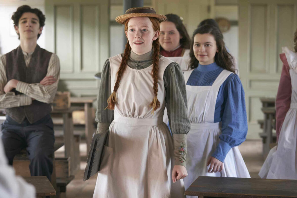 Anne With An E in vintage classroom wearing period attire and straw hat with classmates vintage desks Wallpaper