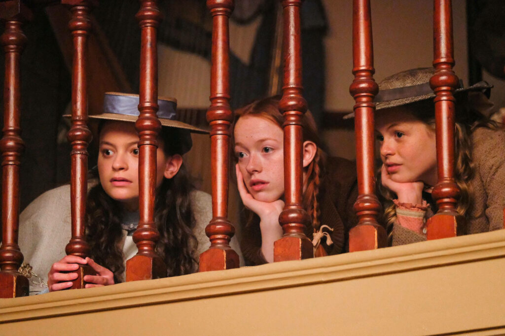 Anne With An E wallpaper shows three girls leaning on wooden railing gazing through balusters