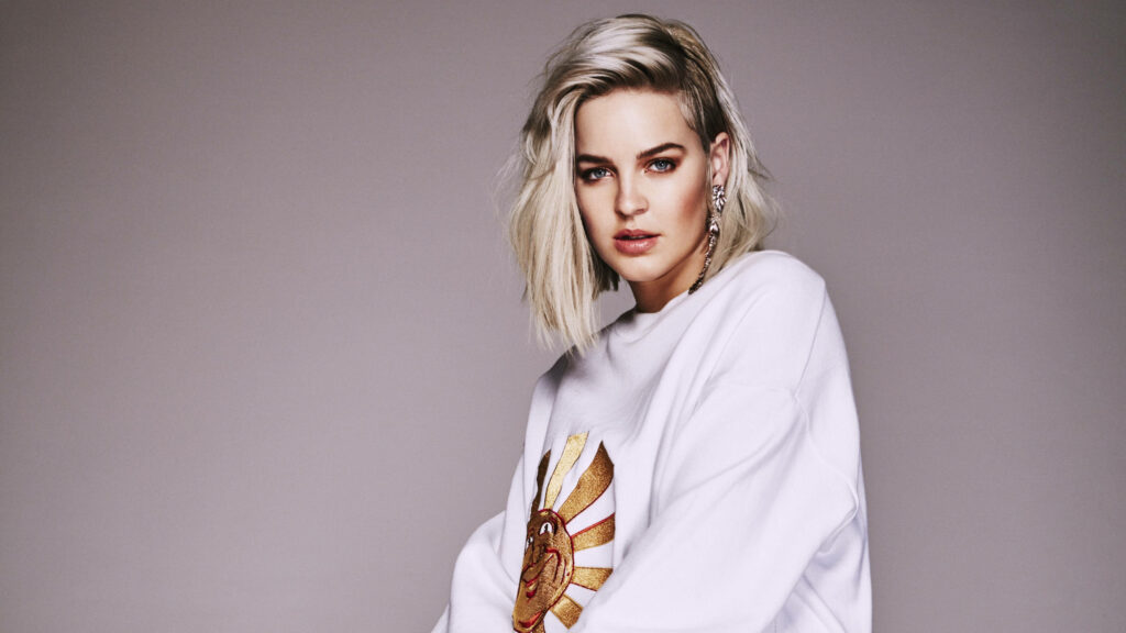 Anne-Marie Nicholson in white sweatshirt posing confidently against grey wallpaper background