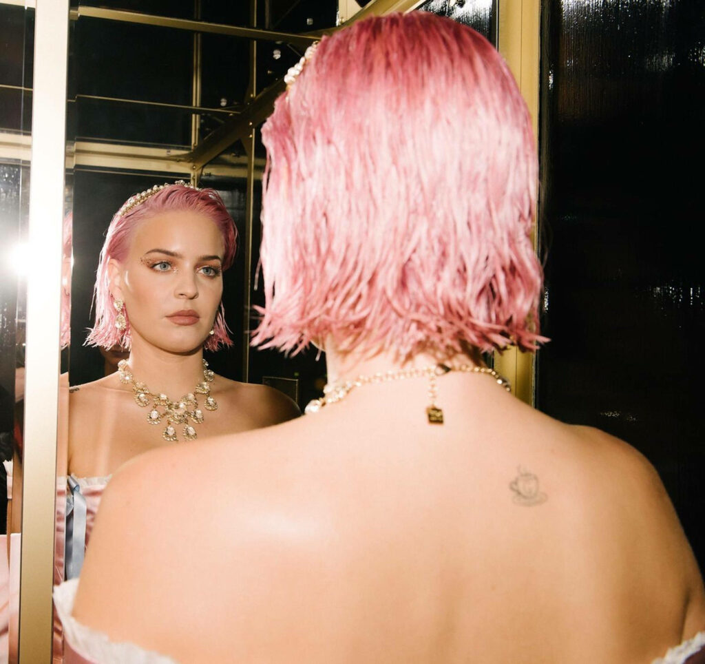 Anne-Marie with pastel pink hair and elegant jewelry gazing thoughtfully at mirror reflection wallpaper
