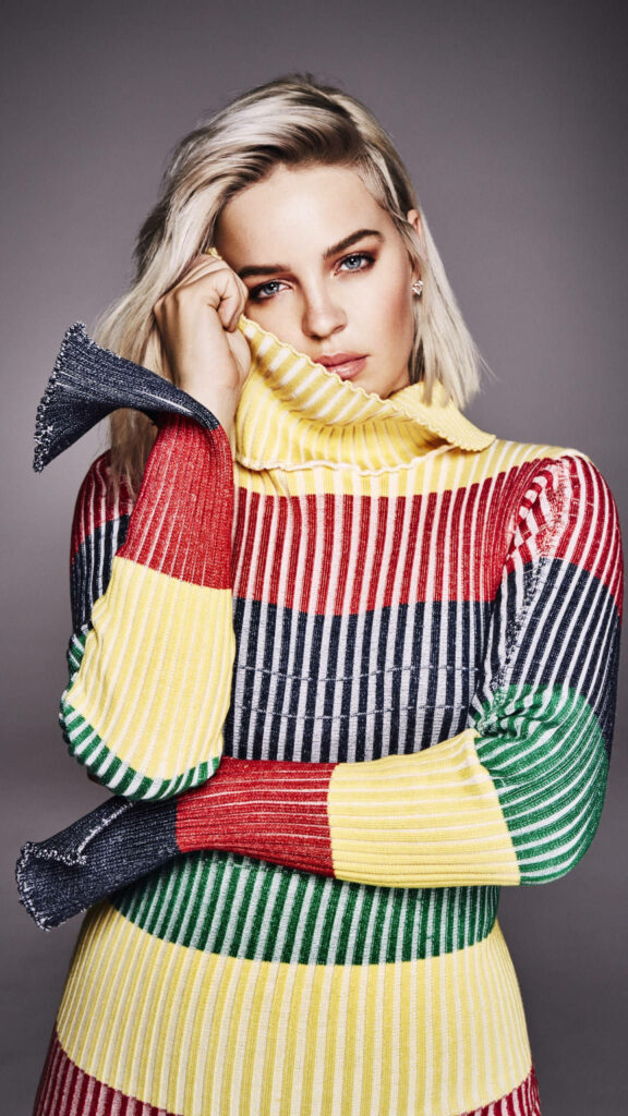 Anne Marie wearing vibrant striped sweater against colorful stylish contemporary wallpaper background