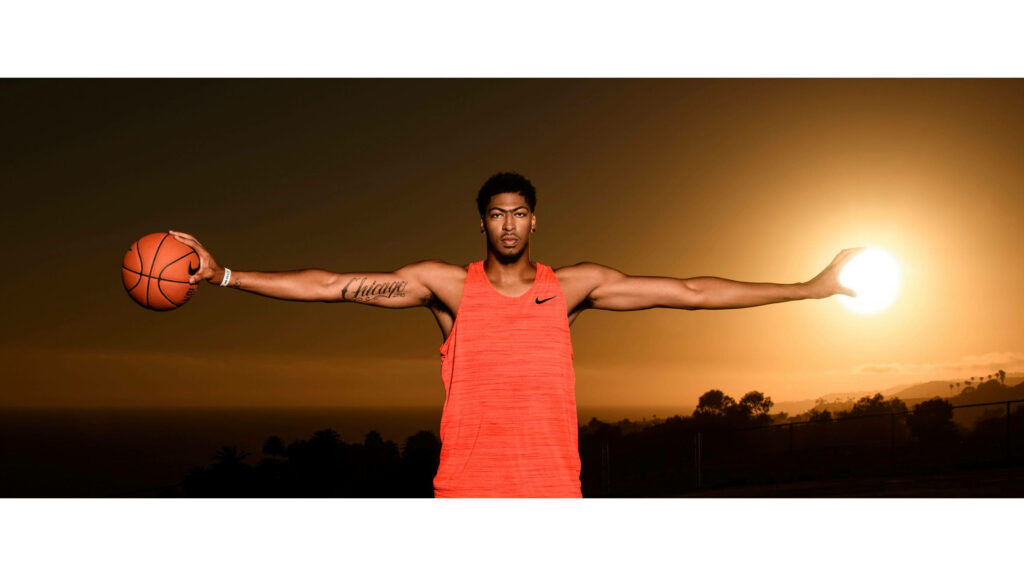 Anthony Davis with basketball and extended wingspan grasping sunset dramatic orange sky wallpaper