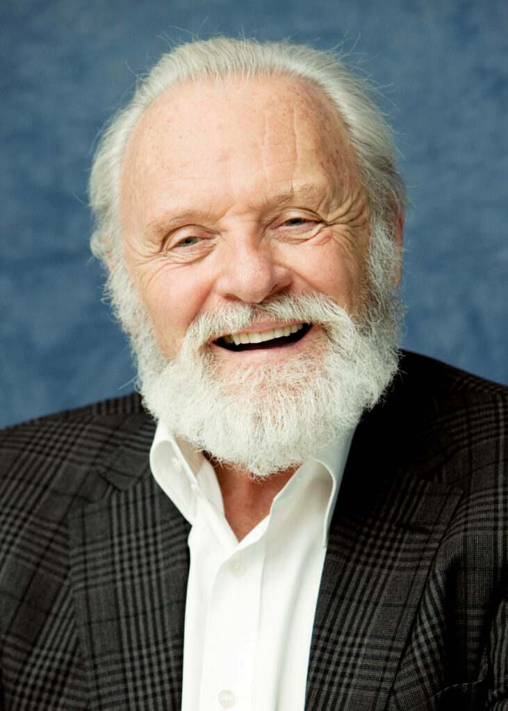 Anthony Hopkins smiling in checkered suit jacket white shirt blue background wallpaper background