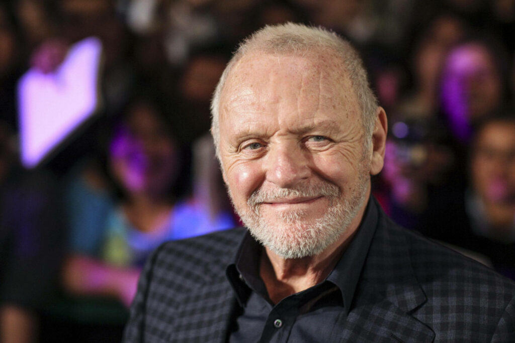 Anthony Hopkins smiling in checkered suit with blurred crowd background cheerful wallpaper