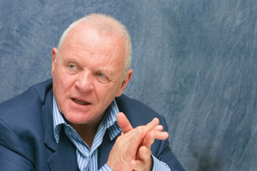 Anthony Hopkins thoughtful portrait sitting against textured blue wallpaper background engaged in conversation