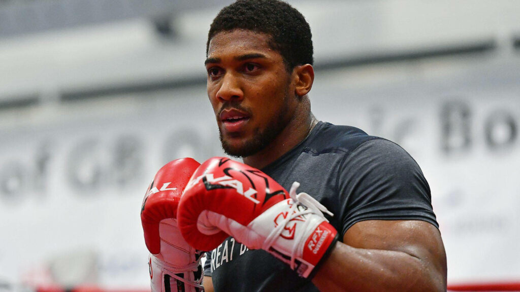 Anthony Joshua training intensely in gym with red boxing gloves showcasing focus and power Wallpaper