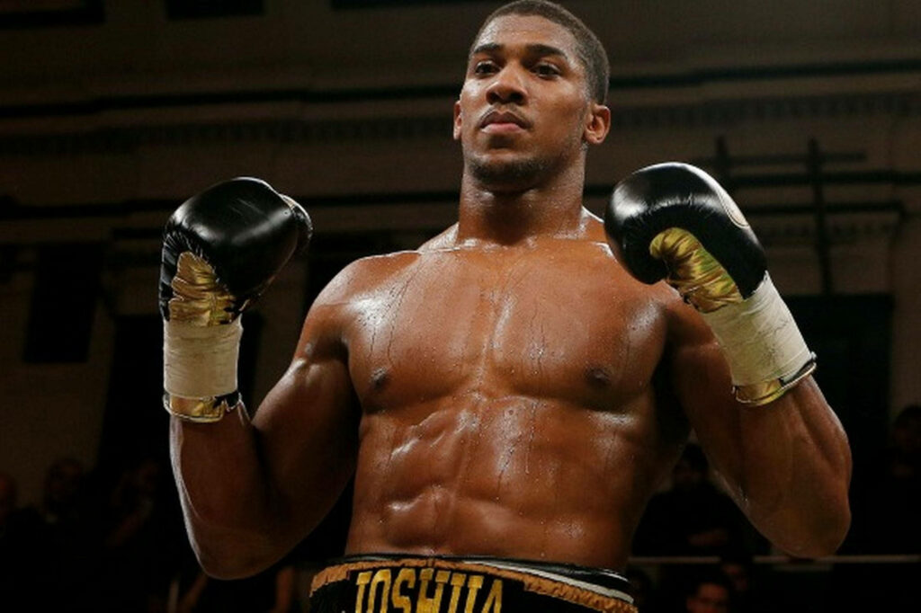 Anthony Joshua in boxing ring with fists raised showcasing muscular physique and fierce determination Wallpaper