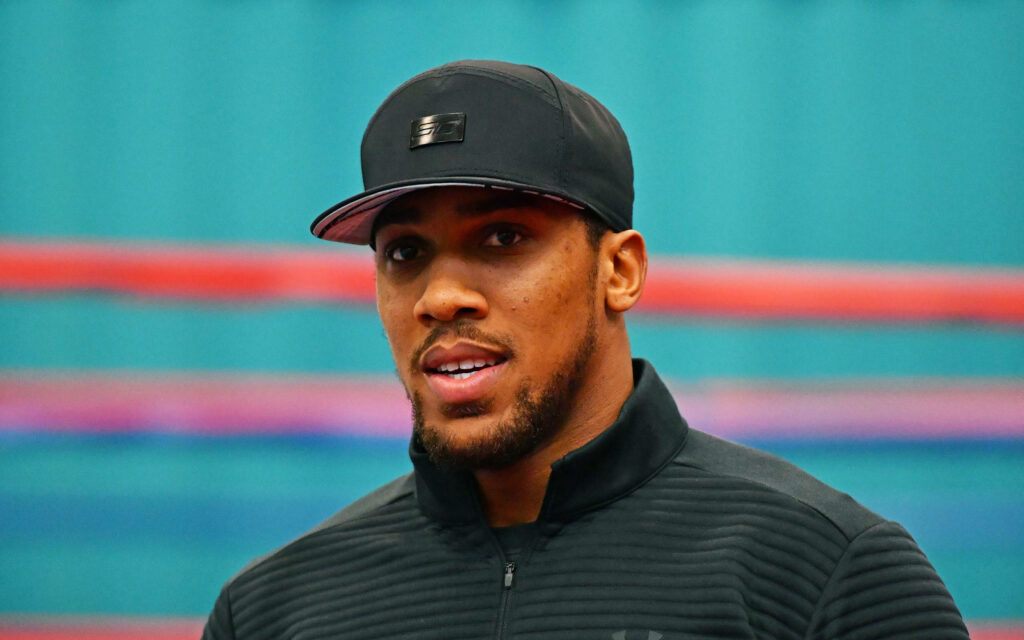 Anthony Joshua focused pose wearing black cap and jacket in front of vibrant green wall background Wallpaper