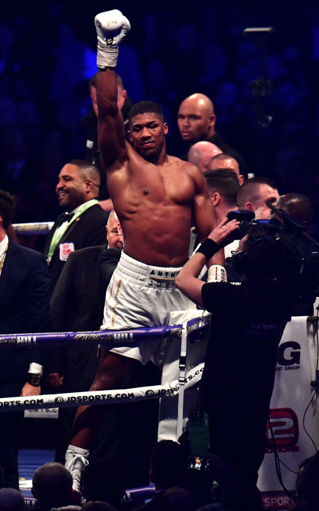 Anthony Joshua celebrates victory in boxing ring with raised hand and cheering crowd background Wallpaper