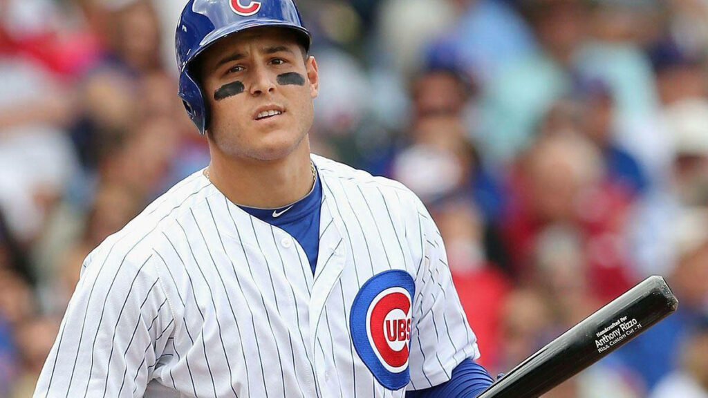 Anthony Rizzo in Chicago Cubs uniform with eye black holding bat on baseball field background Wallpaper