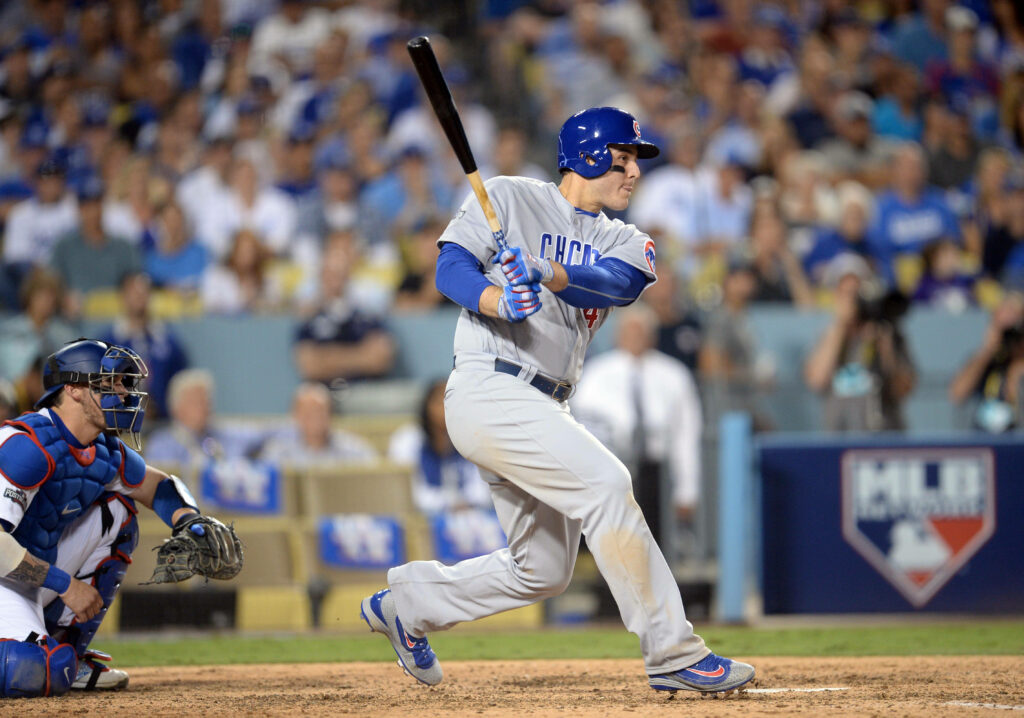 Anthony Rizzo mid-swing running to first base during intense baseball game with crowd background Wallpaper