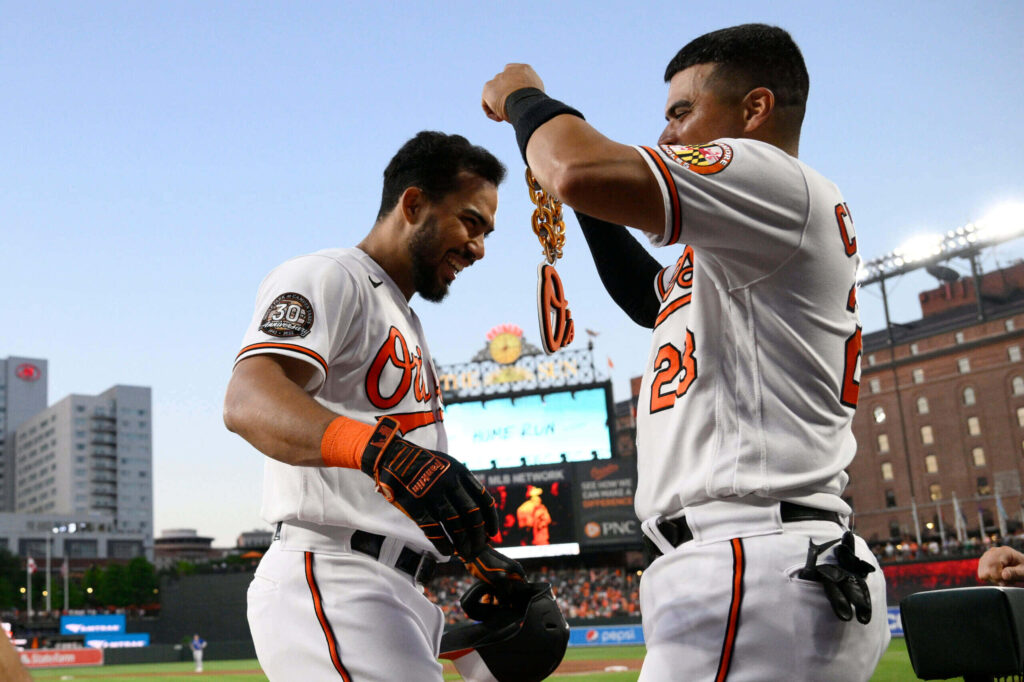 Anthony Santander and Orioles teammate celebrate victory on field displaying large Orioles chain wallpaper