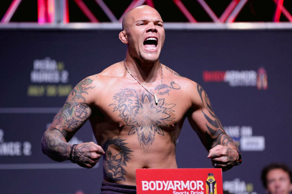 Anthony Smith yelling passionately showing muscular physique and detailed tattoos on stage background Wallpaper