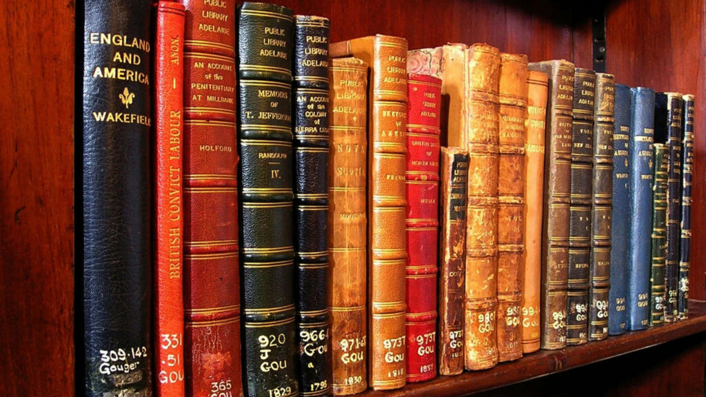 Antique books on polished wooden shelf showcasing historic Adelaide State Library wallpaper background