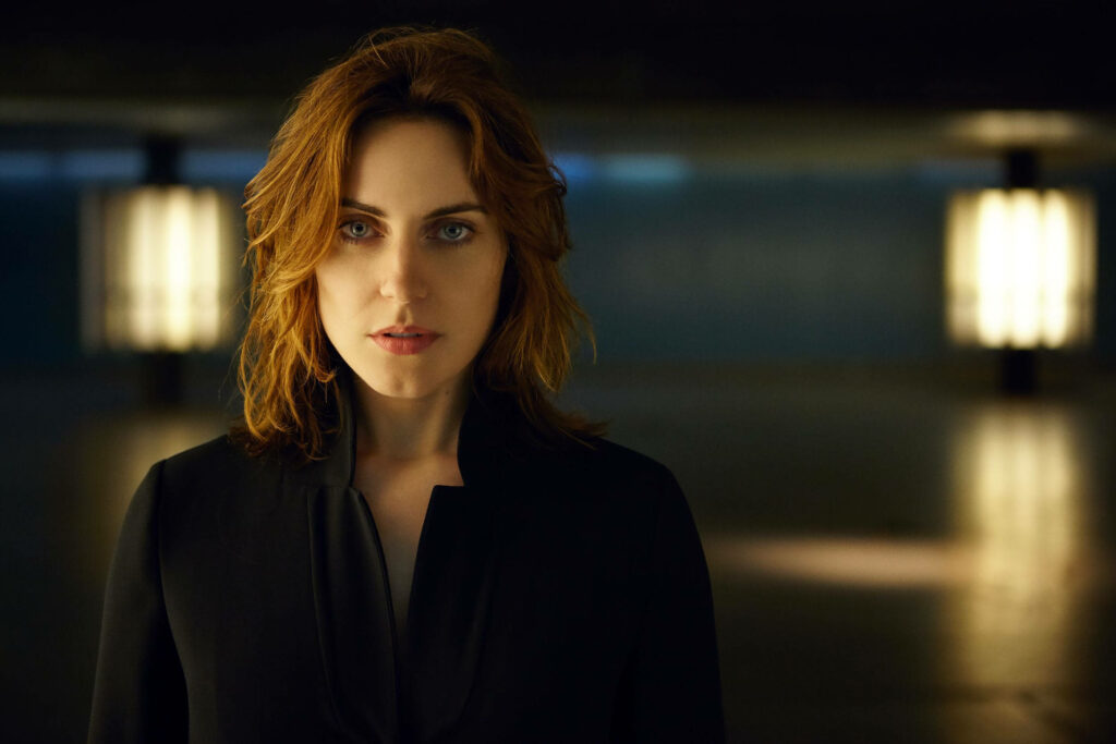 Antje Traue stands confidently in a spacious cozy room with soft lighting and calm atmosphere Wallpaper
