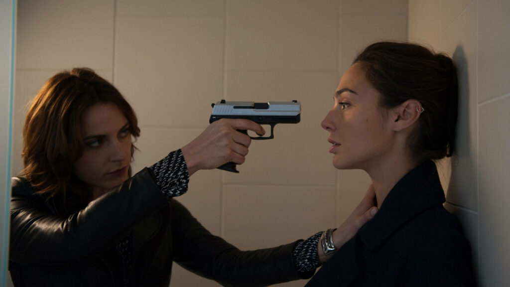 Antje Traue points gun at Gal Gadot in intense dramatic scene wallpaper background tension