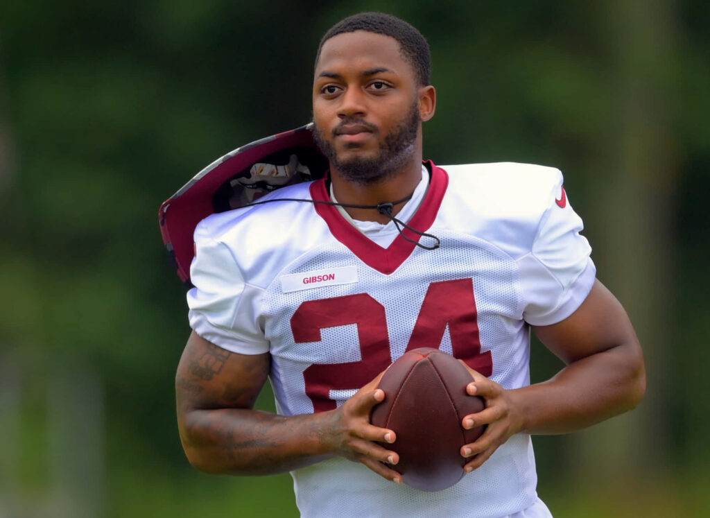 Antonio Gibson focused in football practice uniform holding football during intense training session Wallpaper
