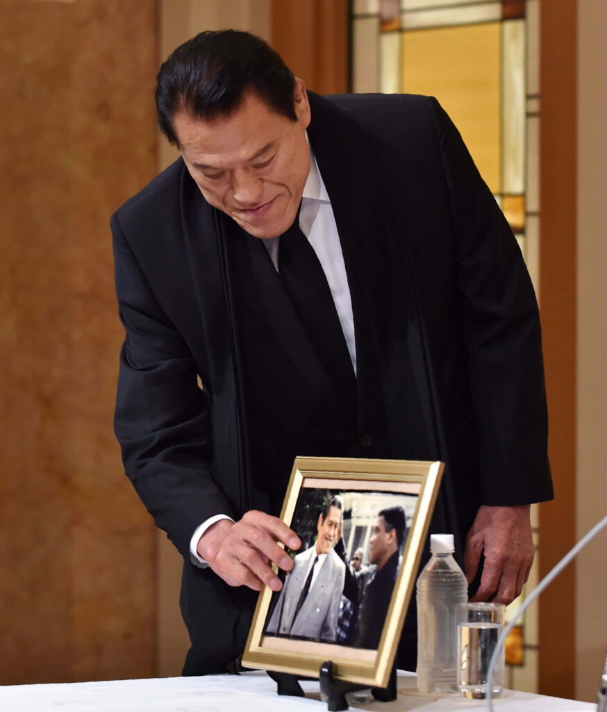 Antonio Inoki arranging framed photograph on table evoking nostalgia in elegant room wallpaper background