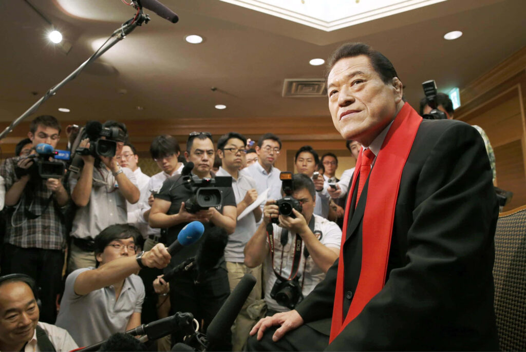 Antonio Inoki at Tokyo press conference surrounded by media photographers iconic wrestling figure Wallpaper