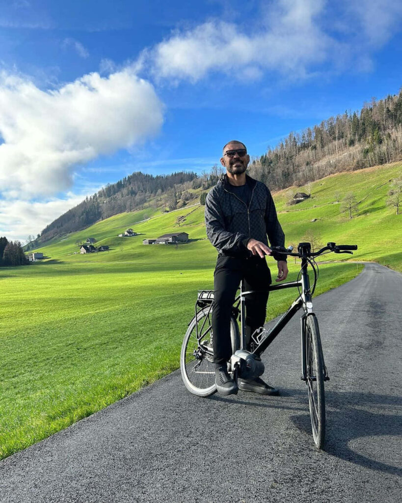 Antônio Rodrigo Nogueira cycling peacefully through lush green mountains under bright blue sky Wallpaper