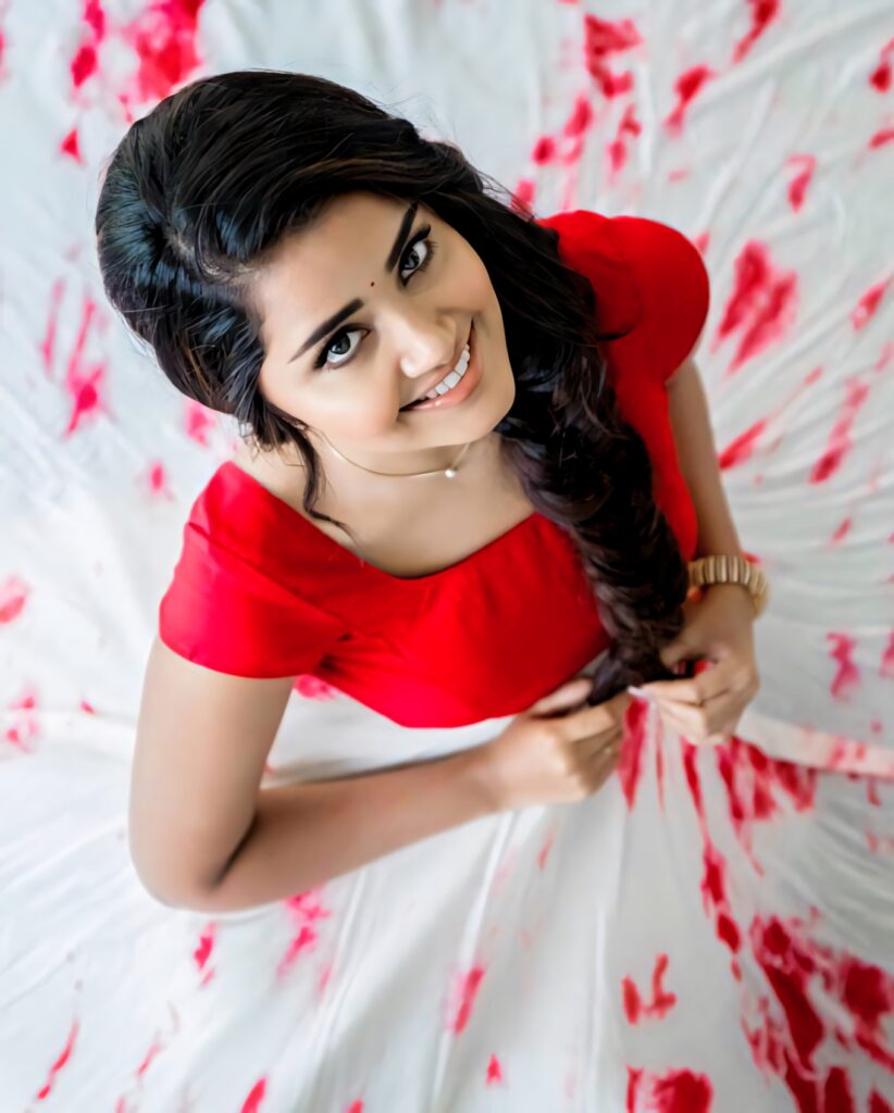 Anupama Parameswaran radiant in red blouse smiling against white and red patterned wallpaper background