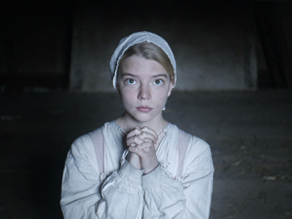 Anya Taylor-Joy in tense scene from The Witch showing innocence vulnerability dimly lit wallpaper