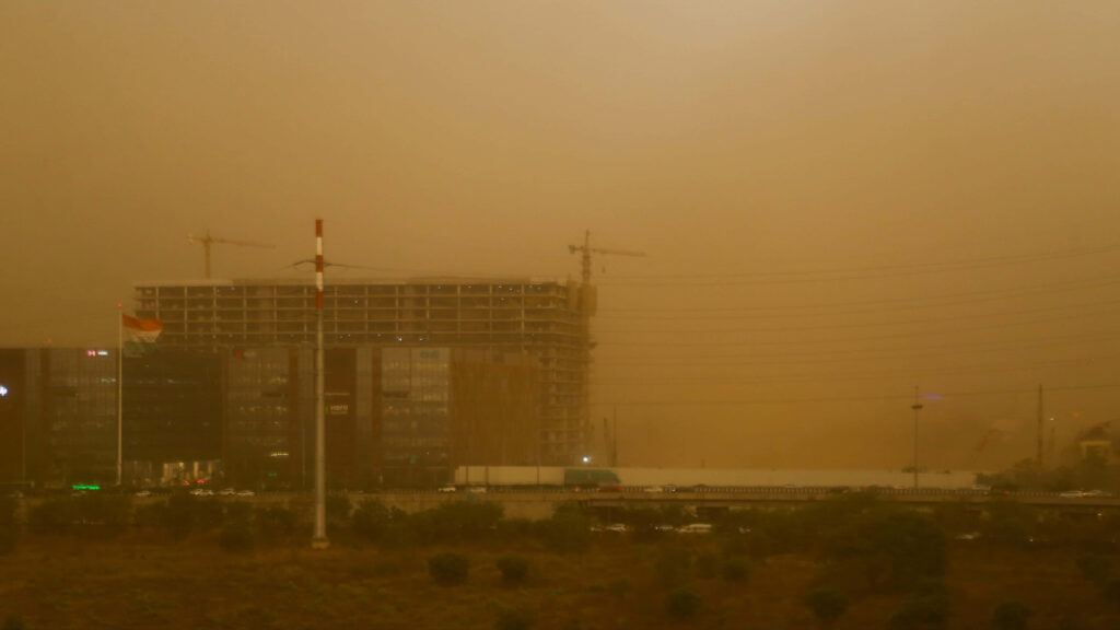 Dust storm engulfs city construction site with amber haze cranes and half-built buildings visible Wallpaper
