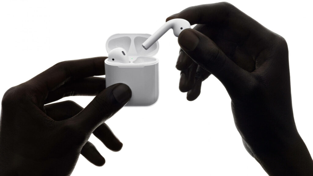 Close-up of hands holding Apple AirPods 2nd Generation with open charging case on white background Wallpaper