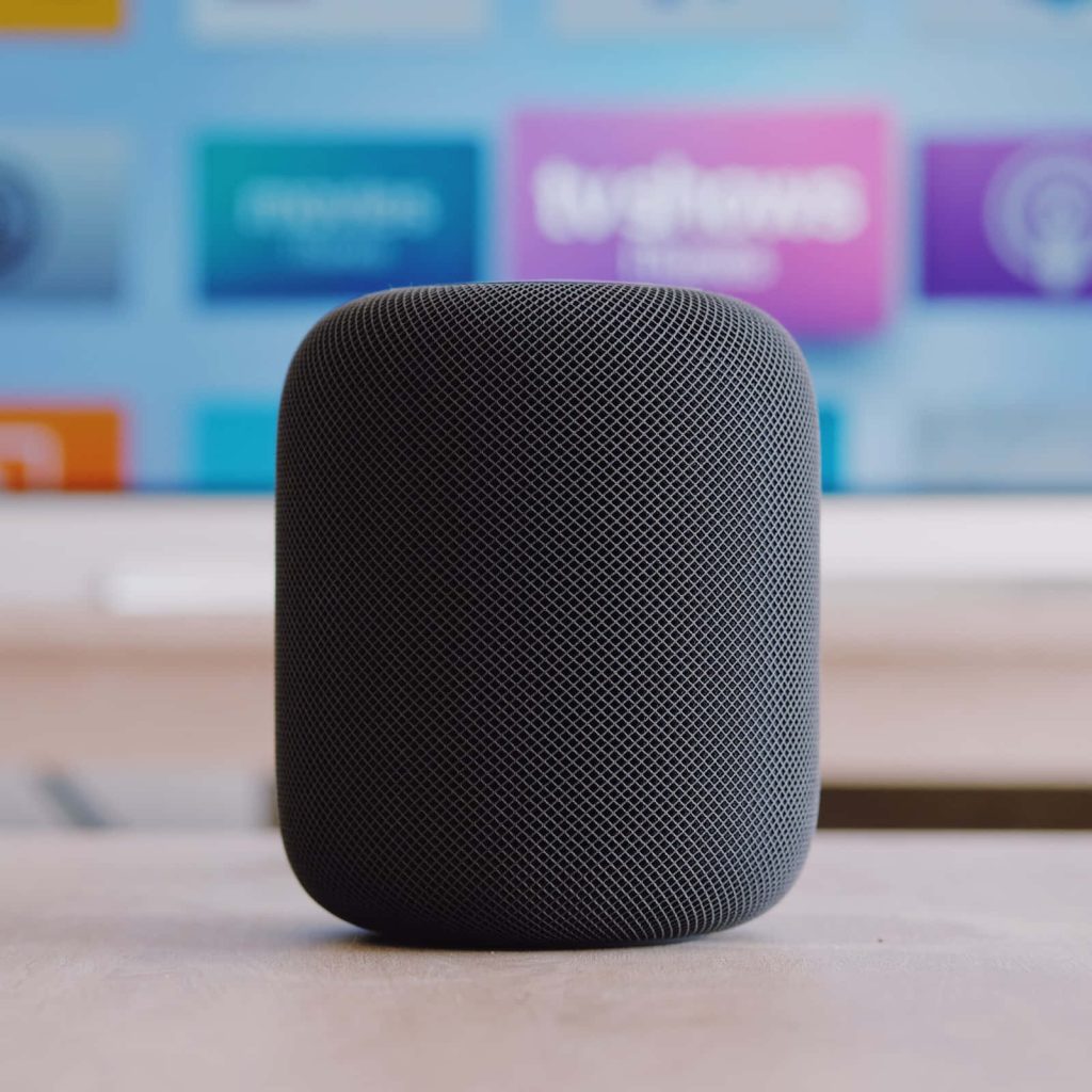 Apple HomePod smart speaker dark grey with mesh texture on light surface colorful blurred background Wallpaper