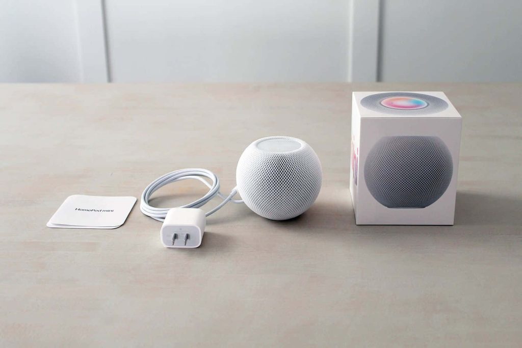 Apple HomePod mini with power adapter packaging and documents on light wood surface background Wallpaper